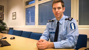 Mikael Appel. Manlig polis sitter vid ett bord omgärdat av kontorsstolar.