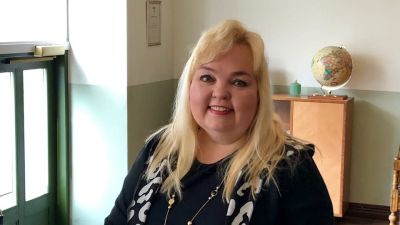 En kvinna med långt blont hår står intill ett bord.
