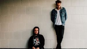 Oskar Nyman (t.h.) och Joel Isaksson bildar duon Hymner. en bild av duon hymner. joel står till höger lutad mot väggen och oskar sitter på marken till vänster med ryggen mot samma vägg.