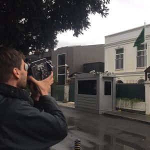 Mies seisoo kadulla ja kuvaa pienellä filmikameralla Saudi-Arabian Istanbulin-suurlähetystön rakennusta. Rakennuksen pihalla on vartiointikoppi ja lippu.