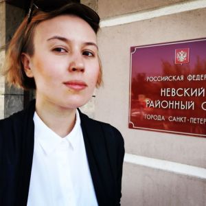 Varvara Michaijlova är jurist och arbetade med Davids fall. Kvinna i vit skjorta och svart kavaj står vid röd skylt där det står något på ryska.