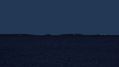 Nattlig vy över havet med blinkande fyrljus.