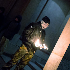 En man som är medlem i Nordiska motståndsrörelsen står med två brinnande facklor i handen i samband med 612-fackeltåget.