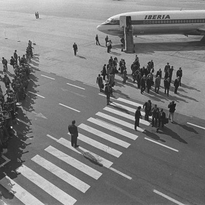 Ulkomaisen vieraan vastaanotto: presidentti Urho Kekkonen kävelee vieraineen kohti lentoasemaa, ympärillä parveilee valokuvaajia, valokuvaajien rivi köyden takana.
