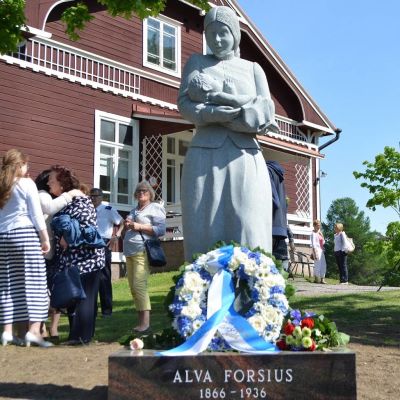 Puutalon edessä on äiti-lapsi-veistos.
