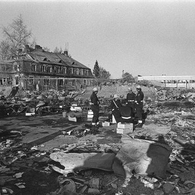 Lapuan patruunatehtaan räjähdyksen raunioita 13.4.1976. Pelastusmiehet istuvat patruunalaatikoilla onnettomuuspaikalla.