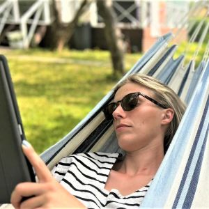 Nainen makaa pihassa riippumatossa aurinkolasit päässä ja selaa iPadia.