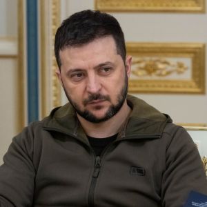 Volodymyr Zelenskyi istuu pöydän takana, sivulla näkyy Ukrainan lippu.