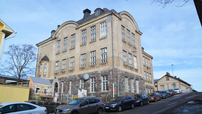 Ett stenhus i flera våningar invid en solbelyst gata.