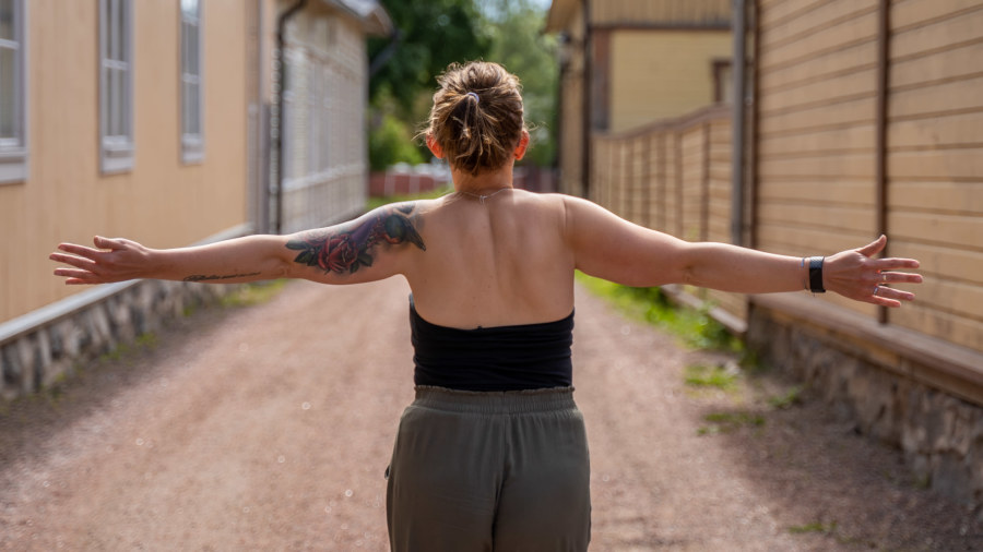 En kvinna går på en gata med trähus med armarna utsträckta.