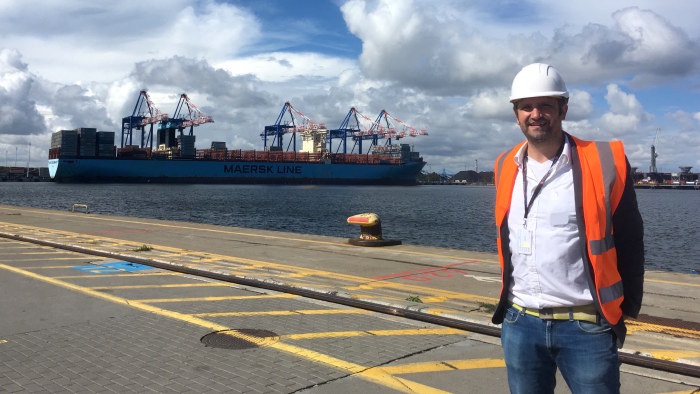 Svenska Yles Gustaf Antell poserar framför ett av världens största fraktfartyg i hamnen i Gdansk.