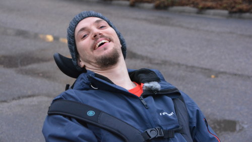 Närbild på Jonas då han lutar sig bakåt i rullstolen och skrattar.