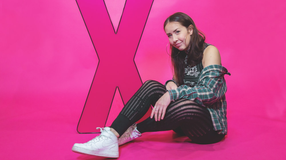 Rap-artisti Adikia istuu maassa X:n muotoisen valokyltin vieressä.