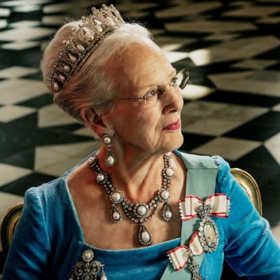 Drottning Margrethe i blå klänning, stort halsband och tiara med pärlor fotograferad i profil. 