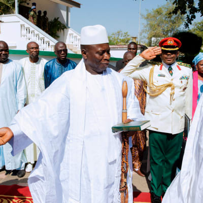 Valkoasuiset Jammeh ja Buhari seisovat ulkona punaisella matolla. Taustalla muita ihmisiä.