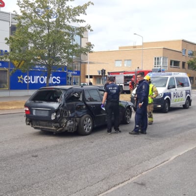 Poliser och brandmän står runt en bil som har krockat i centrum av en stad.