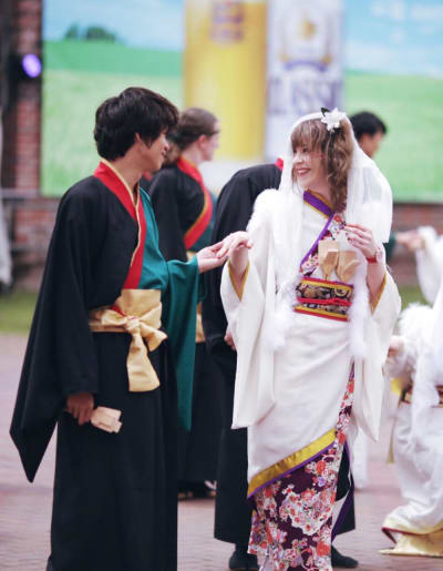 En man och en kvinna som utför den japanska dansen yosakoi. Hon är iklädd vit kimono och han en svart. De håller varandra i handen och ler. 