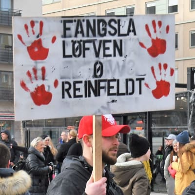 En demonstrant håller en skylt där det står "Fängsla Löfven och Reinfeldt".