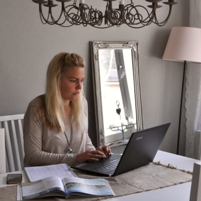 Ela Strandberg sitter vid sitt vita matbord hemma vid sin dator.