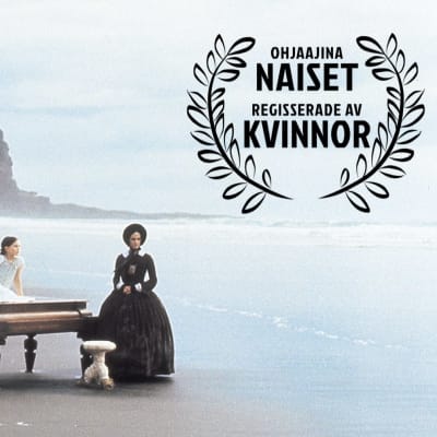 Nainen ja tyttö ja piano autiolla rannalla. Kuvassa iso Ohjaajina naiset -logo. Kuva elokuvasta Piano.