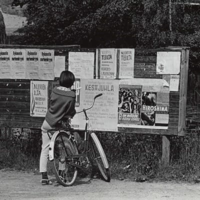 Flicka och cykel framför annonstavla