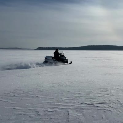 Moottorikelkka kiitää järven jäällä aurinkoisena talvipäivänä.