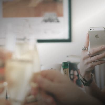 Några händer som håller i glas skålar medan en hand håller i en smarttelefon och fotar händelsen.