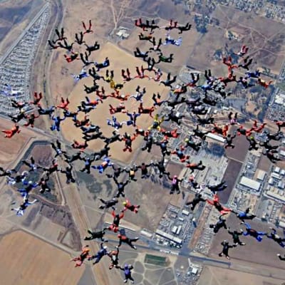 130 fallskärmshoppare faller i en snöflingeformation högt över marken.