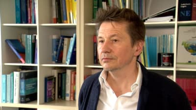 Professor Alex Housen fotograferad i sitt arbetsrum i Bryssel. I bakgrunden syns en bokylla med facklitteratur. 