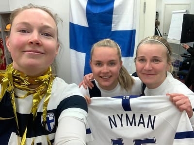 Sanni Franssi, Iina Salmi och Anna Auvinen håller upp Linda Nymans spelskjorta.