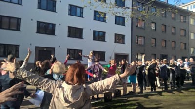 Parikymmentä ihmistä helsinkiläisellä kadulla tekemässä äänenavausta kädet sivuille levitettyinä.