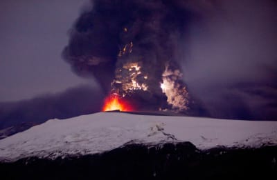 Jäätikön alta purkautuvasta tulivuoresta räiskyy oranssipunaista laavaa ja nousee paksu hiukkaspilvi yötaivaalle.