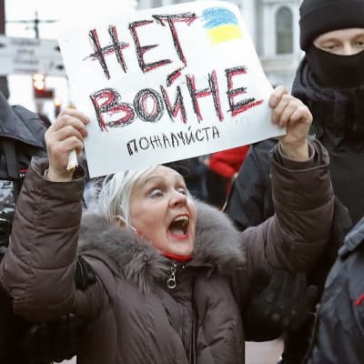 En kvinna med en skylt där det står нет войне (nej till krig) omringas av tre poliser på en demonstration i S:t Petersburg.