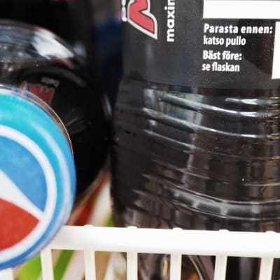 Två pepsiflaskor på en hylla: den ena ligger ner med Pepsicos logotyp mot tittare, den andra står och man ser texten Bäst före: se flaskan.