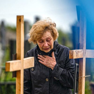 En kvinna står framför en rad gravar. Bredvid gravarna vajar Ukrainas flagga.