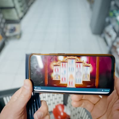 En man håller en telefon i handen och spelar på ett nätkasino i en matbutik.