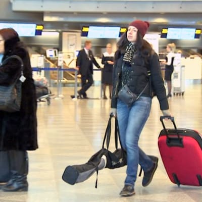 Nainen kulkee lentokentällä suksipussin ja matkalaukun kanssa.