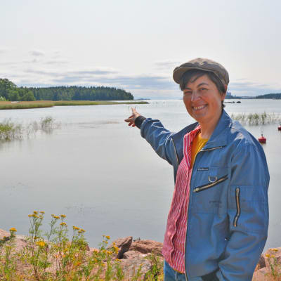 En kvinna står och pekat mot en punkt ute på vattnet i en vik.