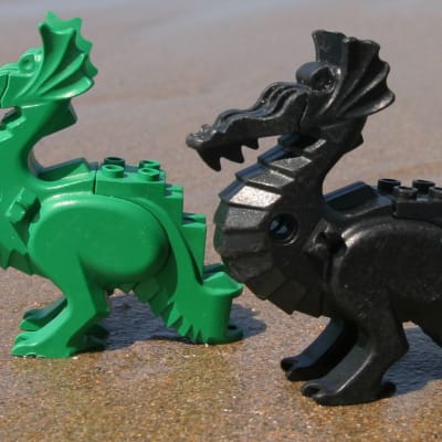 Två legodrakar, en grön och en svart, på en sandstrand.