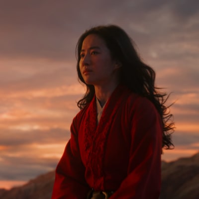 Närbild på Mulan (Yifei Liu) sitter på ett berg i solnedgången.