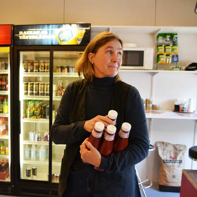 En kvinna står inne i en bybutik. Hon håller i ketchupflaskor.