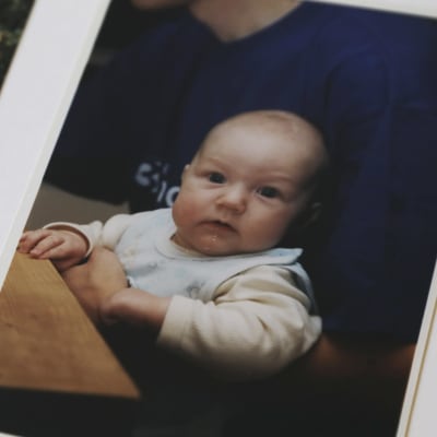 Kuvassa valokuva-albumi, jossa vauvan kuva, vauva katsoo kameraan.
