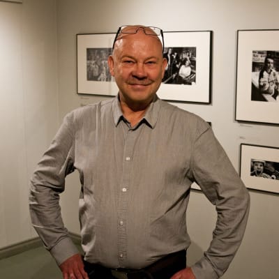 Valokuvaaja Olli Herranen poseeraa, taustalla Herrasen KalPa-aiheisen valokuvanäyttelyn satoa.