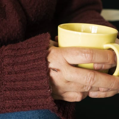 Kuvassa naisen kädet, ja käsien välissä kahvimuki