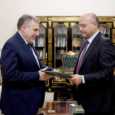 Iraks president Barham Salih (till höger) utser Mohammad Allawi (till vänster) till Iraks nya premiärminister. På bilden står männen framför en bokhylla och Iraks flagga.