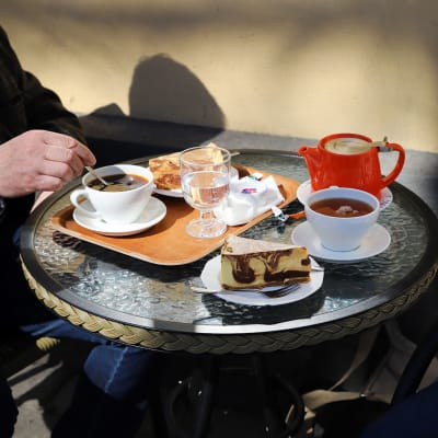 Två personer sitter vid ett kafébord med var sin kaffe och tårtbit.
