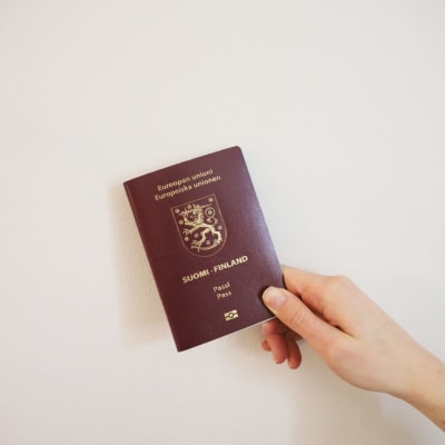 En hand håller i ett finskt pass mot en ljus vägg.