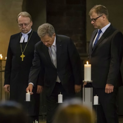 President Saulli Niinistö tänder ett ljus under minnesstund för offren i inbördeskriget. Statsminister Juha Sipilä, ärkebiskop Kari Mäkinen och Vänsterförbundets riksdagsledamot Li Andersson står intill. 
