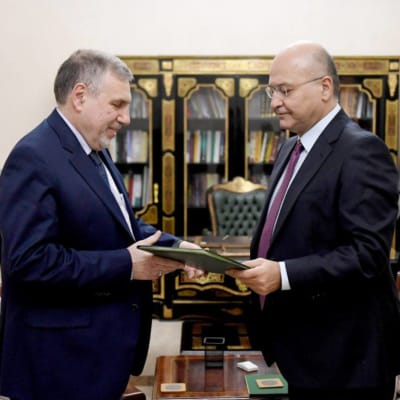 Iraks president Barham Salih (till höger) utser Mohammad Allawi (till vänster) till Iraks nya premiärminister. På bilden står männen framför en bokhylla och Iraks flagga.