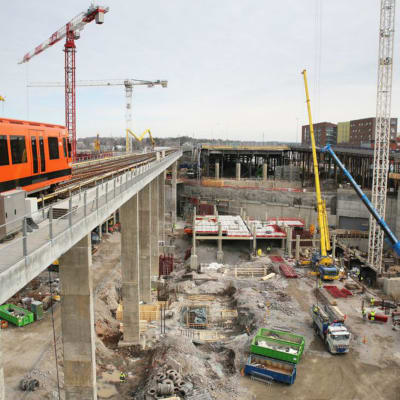 En orangefärgad metro kör förbi byggplatsen med lyftkranar vid Fiskehamnen i Helsingfors.